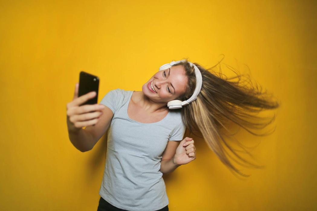 Girl wearing heaphones and looking at phone.